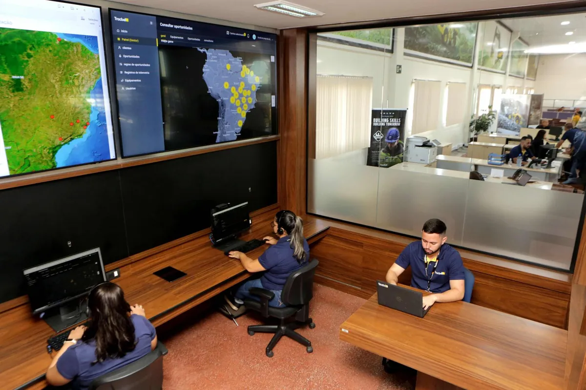 Tracbel monitoring center: operators at their desks in front of wall screens with a map of Brazil.